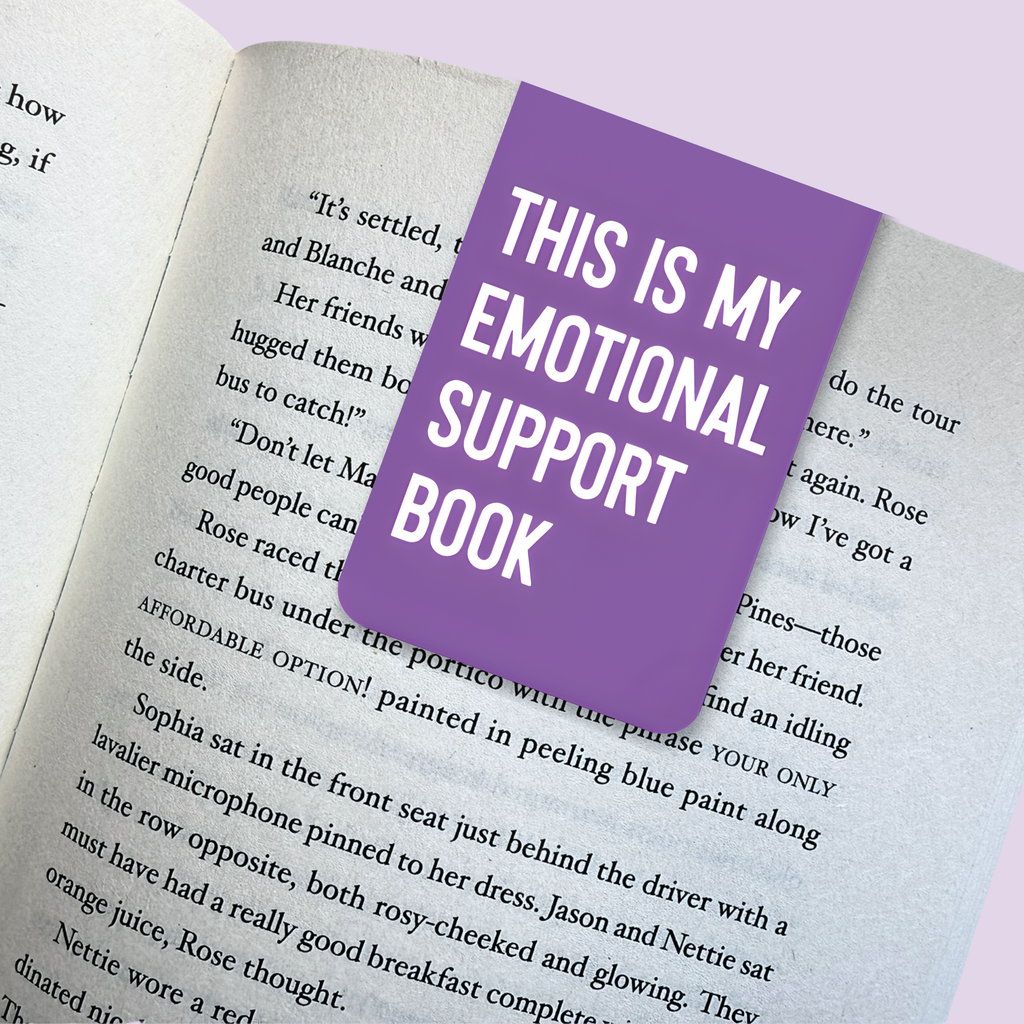 Open book with a purple bookmark reading 'This is my emotional support book' on a light purple background.